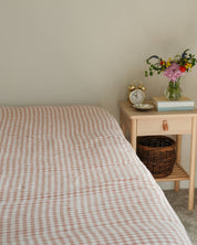 Bed with checkered bedding next to a wooden nightstand with a clock and flowers.