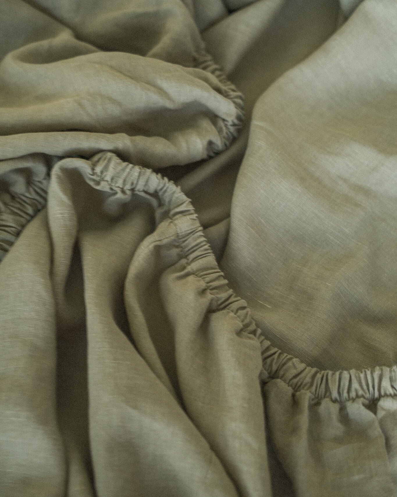 Close-up of sage green linen fitted sheet with elastic band